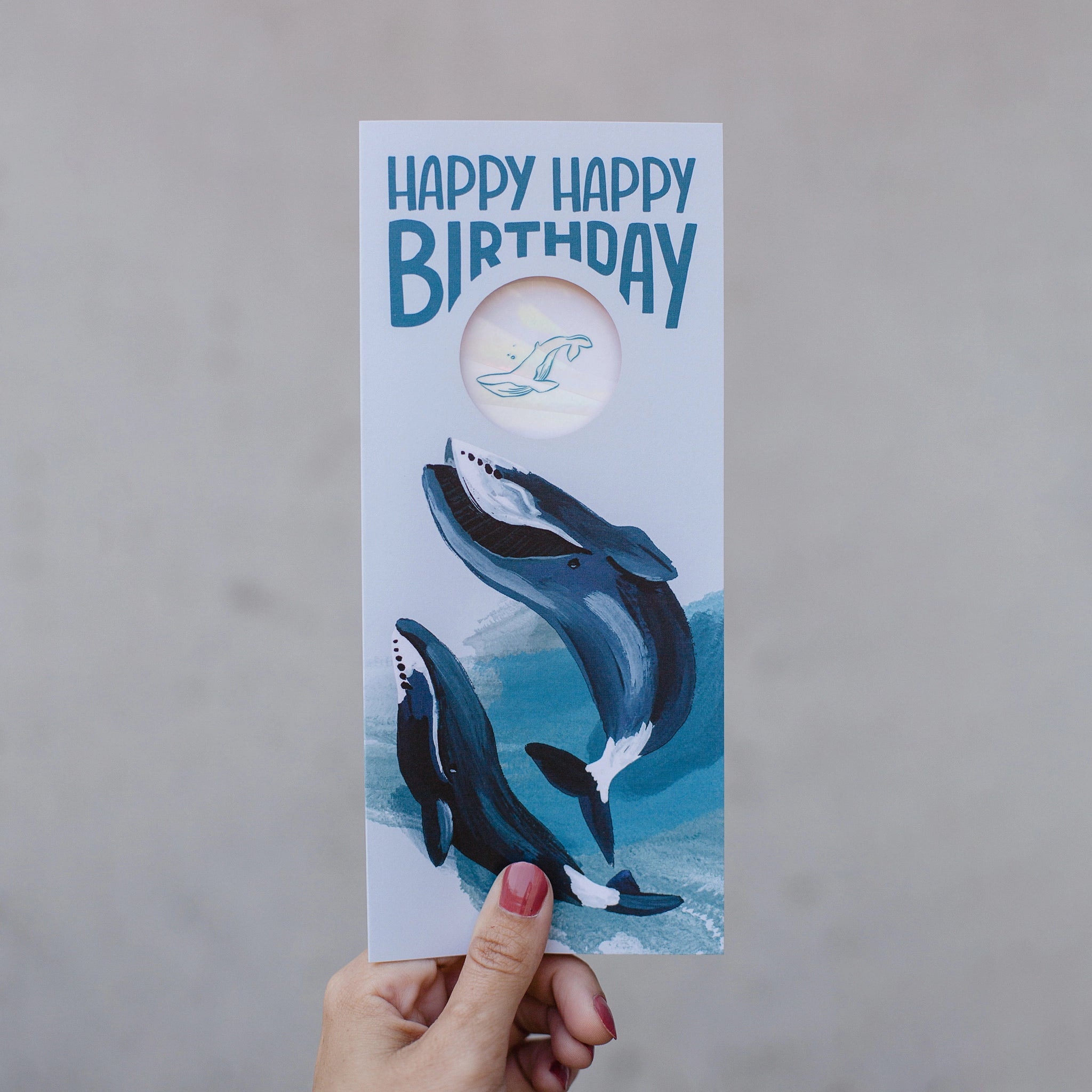 No. 10 greeting card with a suncatcher sticker included. Front: Two swimming whales with the words "Happy happy birthday." The colors are shades of blue. There is a cutout window that shows the suncatcher sticker included inside.